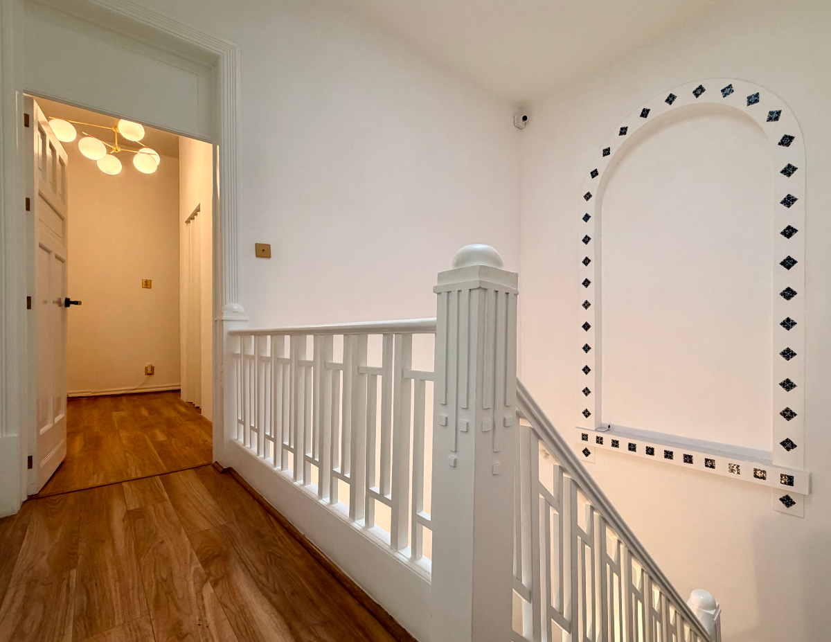 Serene studio landing with white geometric railing, black tile detailing, and warm ambient lighting.